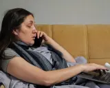 Kobieta w łóżku, rozmawiająca przez telefon i pracująca na laptopie, zastanawia się, na ile dni opłaca się brać zwolnienie lekarskie.
