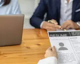 Osoba przegląda CV, na którym widnieje sekcja "Umiejętności twarde". Obok leży laptop.
