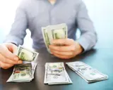 Mężczyzna liczy banknoty 100-dolarowe, symbolizujące dobrze płatne zawody i sukces finansowy.